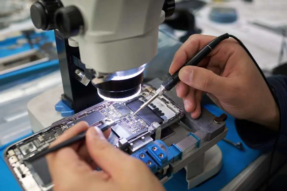 Técnico realizando micro solda em placa de smartphone sob microscópio em bancada de assistência técnica