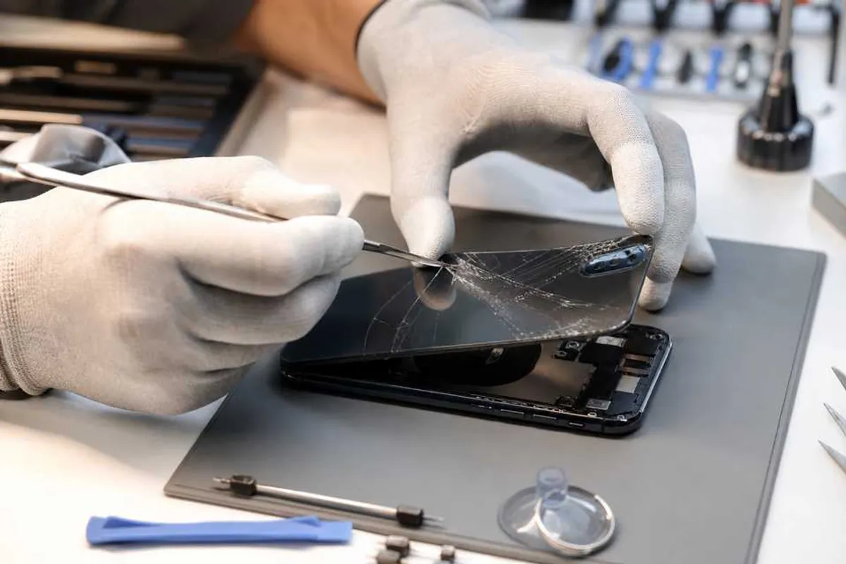 Técnico substituindo a tampa de vidro traseiro trincada de um smartphone em bancada de assistência